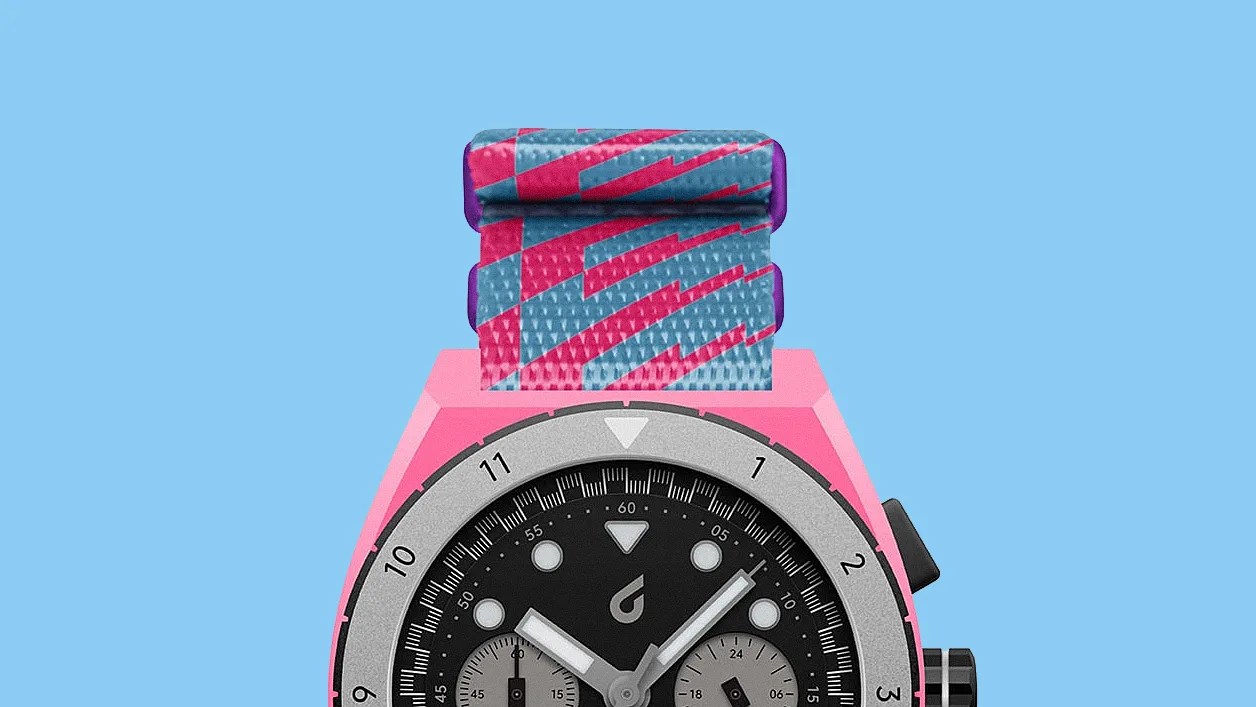 Close-up of a wristwatch with a pink case, black dial, silver bezel, and a blue and pink patterned fabric strap against a blue background.