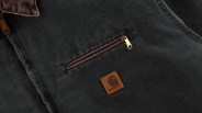 Dark green fabric with a brown zipper and a square Carhartt leather logo patch.