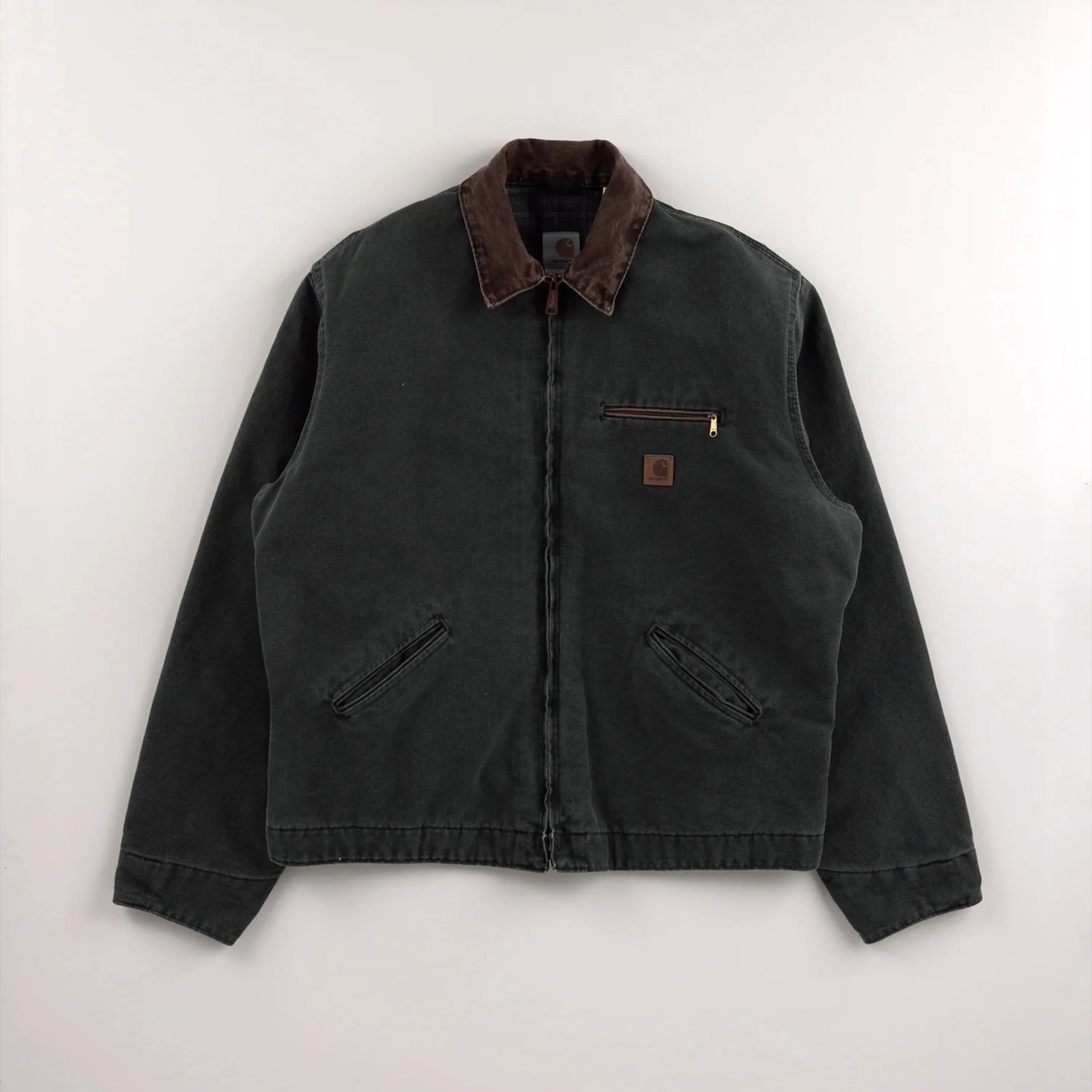 Dark green Carhartt jacket with brown corduroy collar and zippered chest pocket on a white background.