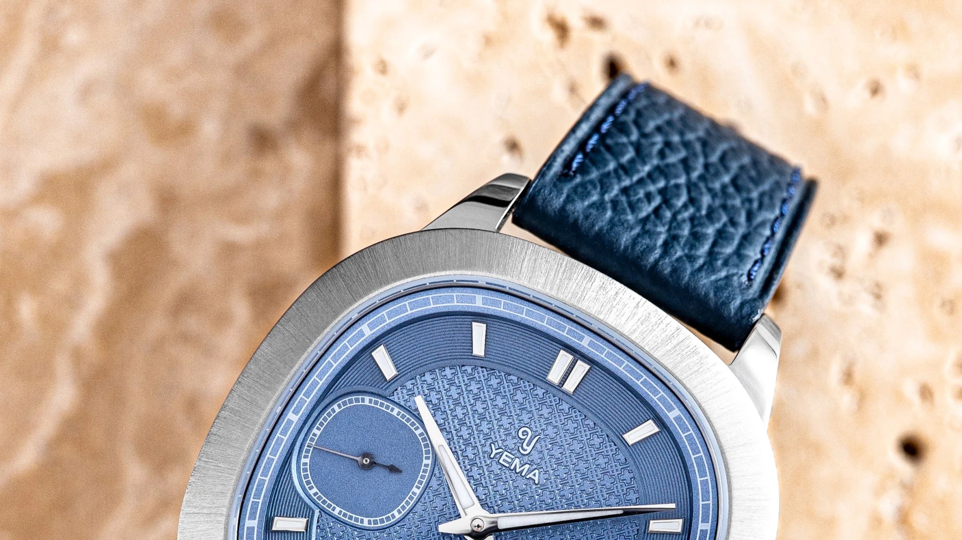 Close-up of a Yema wristwatch with a textured blue dial, silver markers, and a blue leather strap.