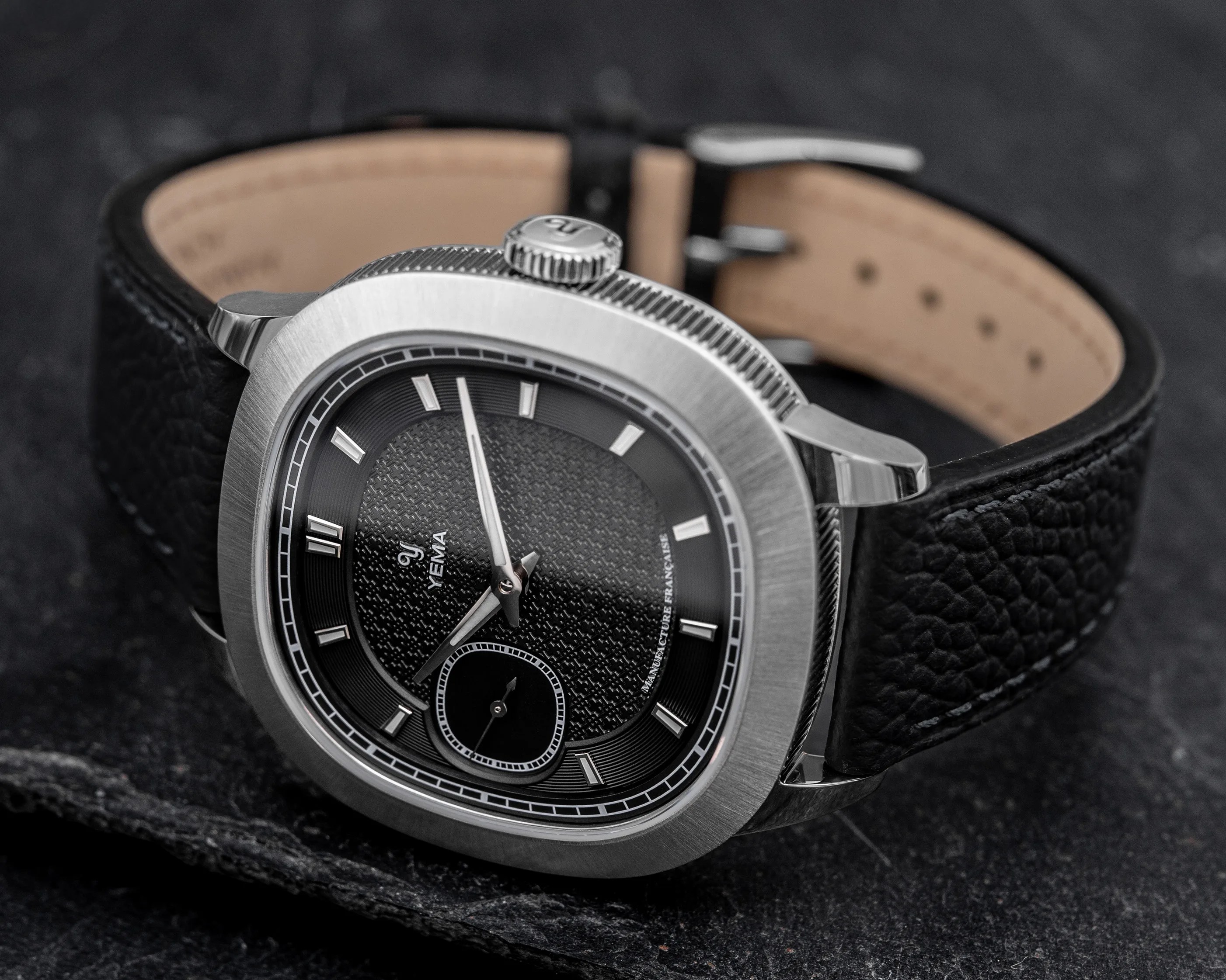 Close-up of a Yema wristwatch with a textured black dial, silver markers, and a black leather strap.