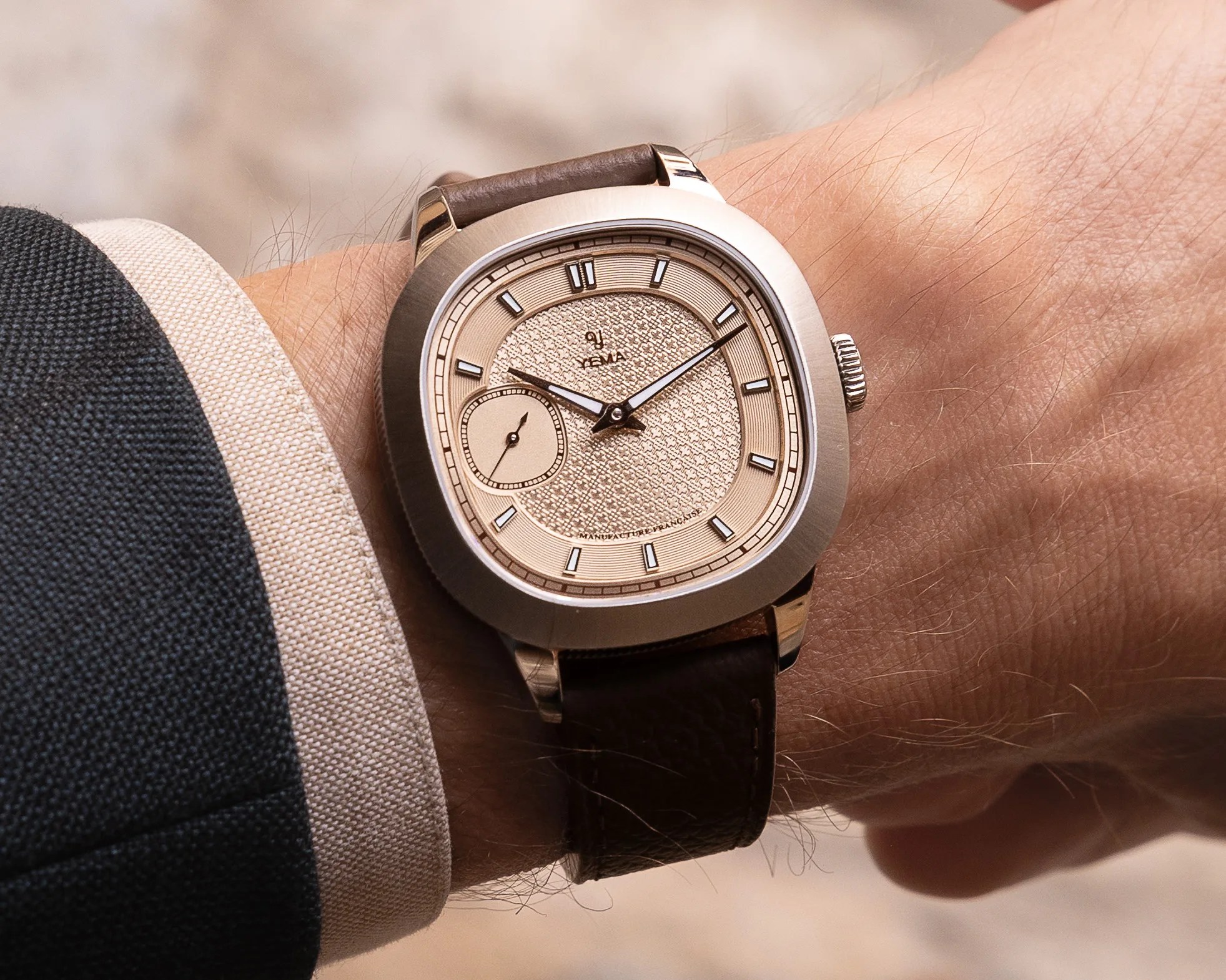 Silver-toned wristwatch with textured beige dial, brown leather strap, and small seconds subdial worn on a wrist.