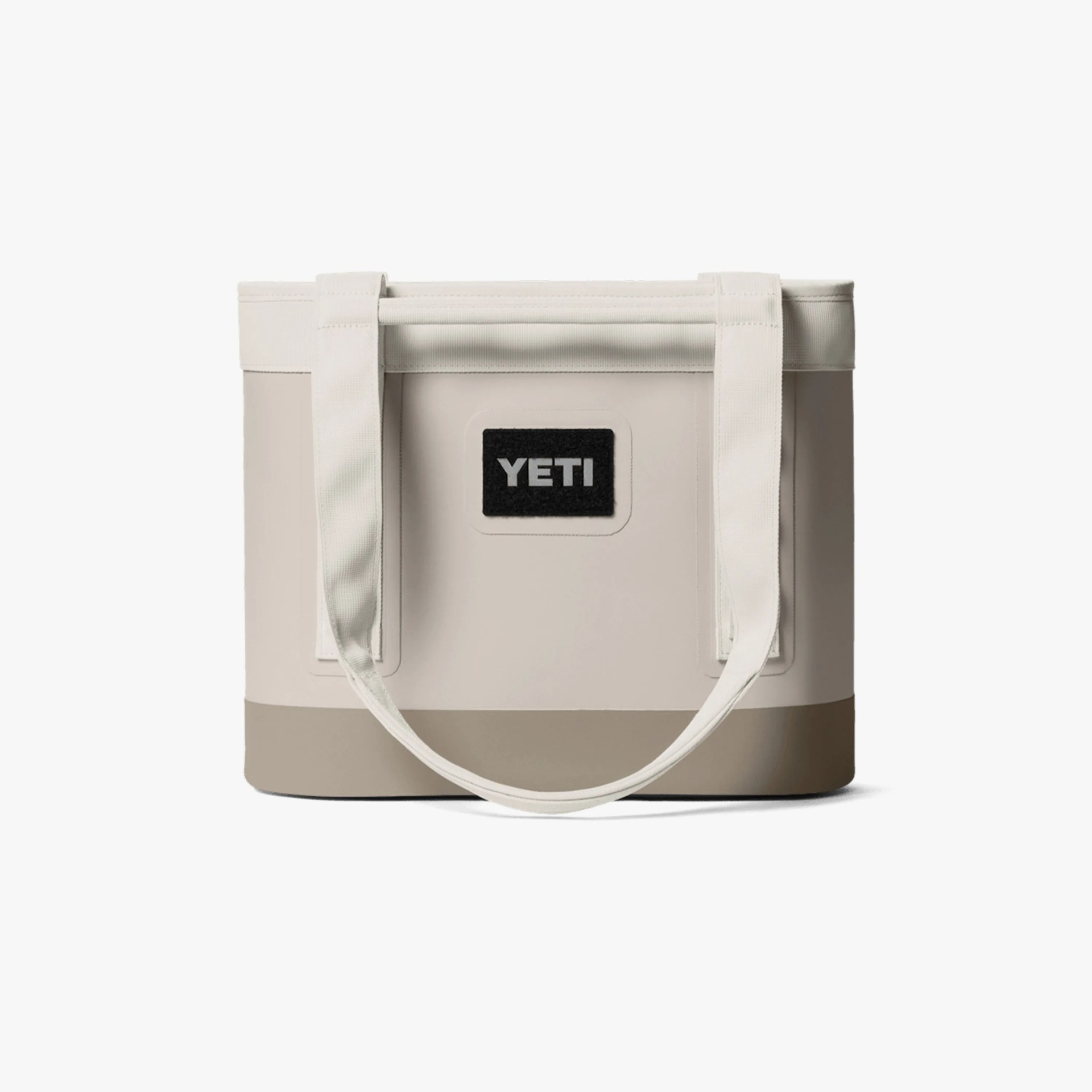 Beige and tan YETI tote bag with white handles and a black logo patch on the front.