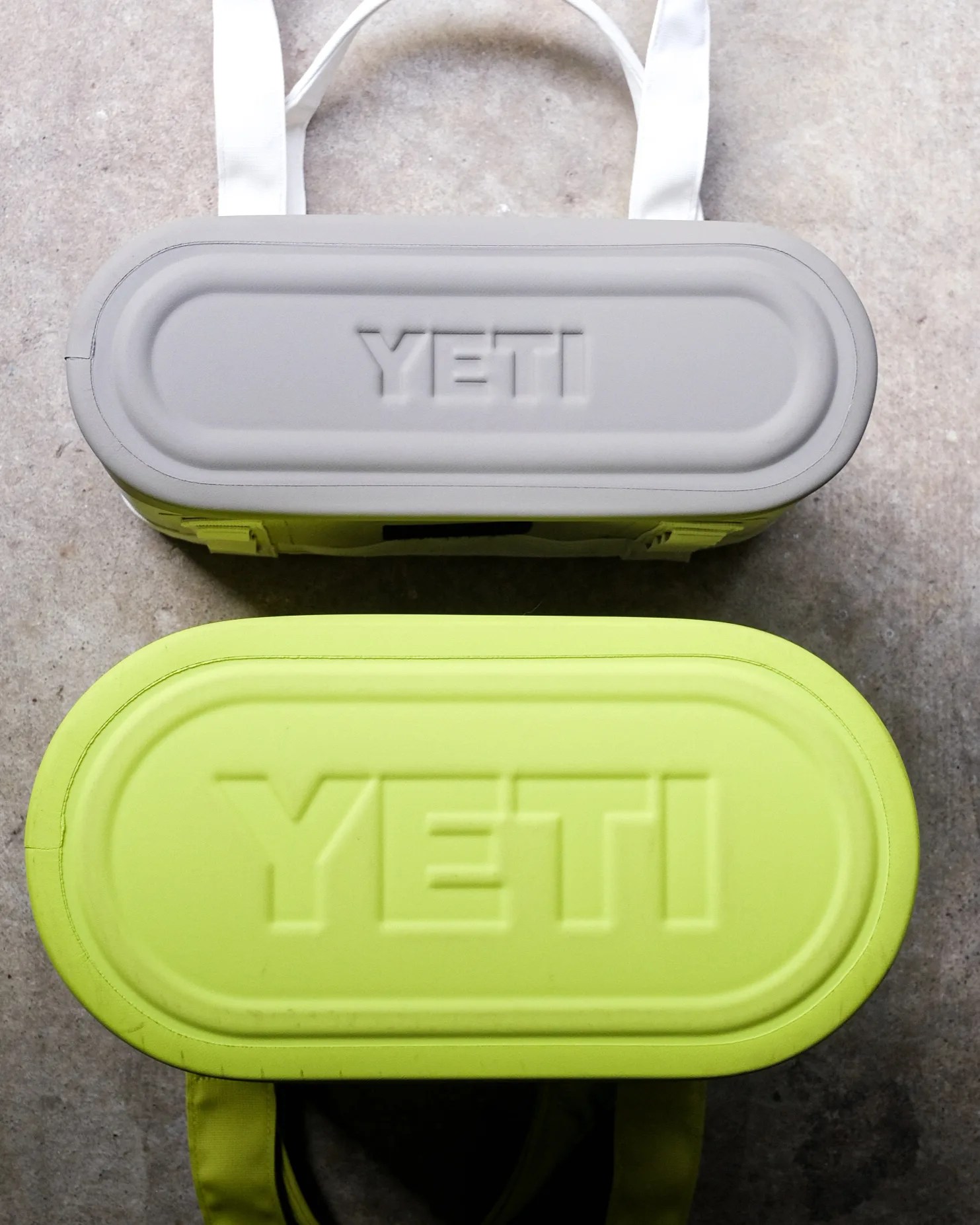 Top view of two YETI coolers, one gray with white straps and one lime green, on a concrete surface.