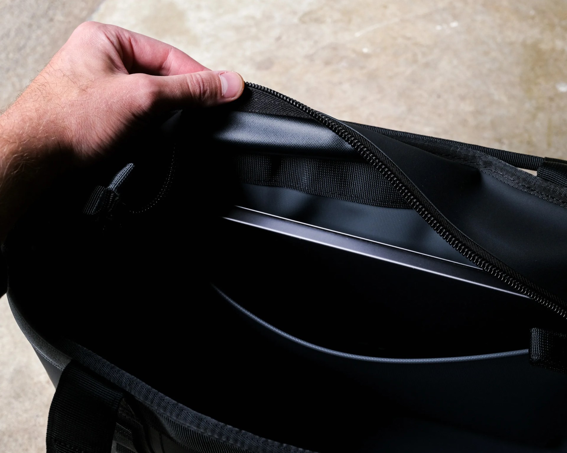 Hand holding open the zipper of a black laptop bag with a laptop inside.