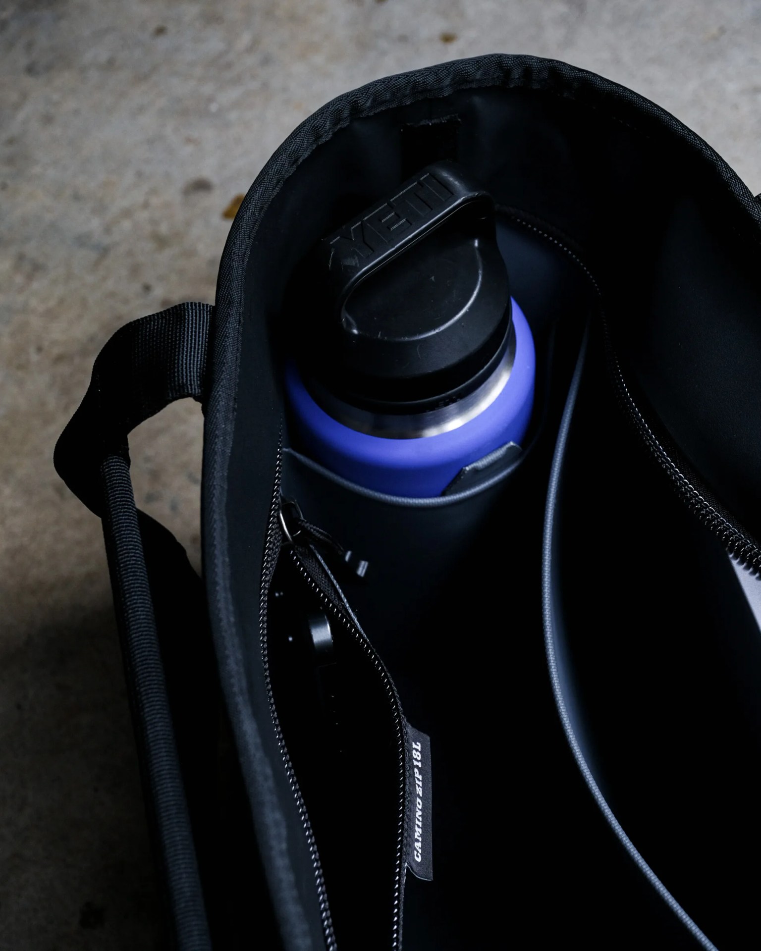 Black insulated bag with a blue YETI water bottle inside a side pocket.