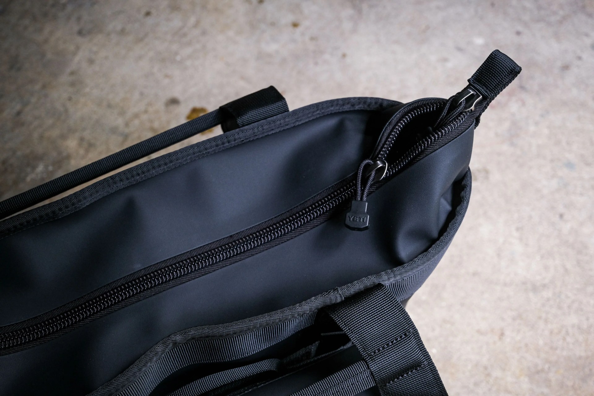 Close-up of a black bag with a partially open zipper and a YETI-branded zipper pull.