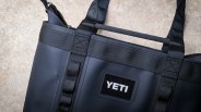 Close-up of a black YETI bag with reinforced straps and a zipper on a concrete surface.