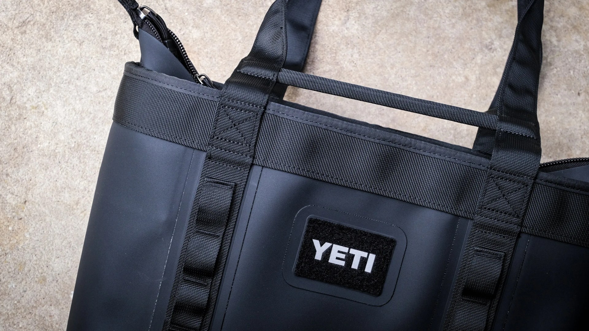 Close-up of a black YETI bag with reinforced straps and a zipper on a concrete surface.