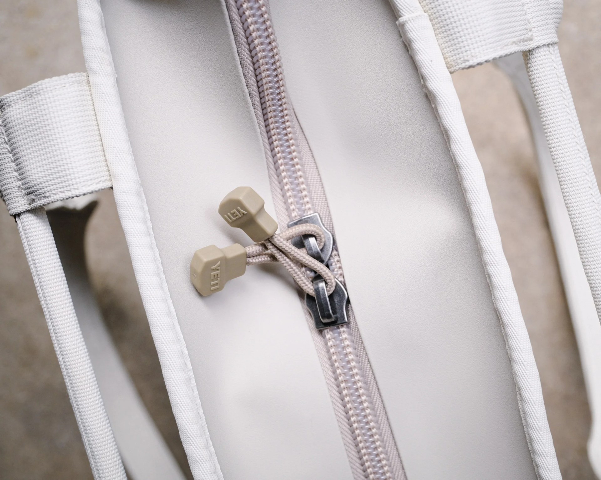 Close-up of a beige zipper with YETI-branded pull tabs on a light-colored fabric bag.
