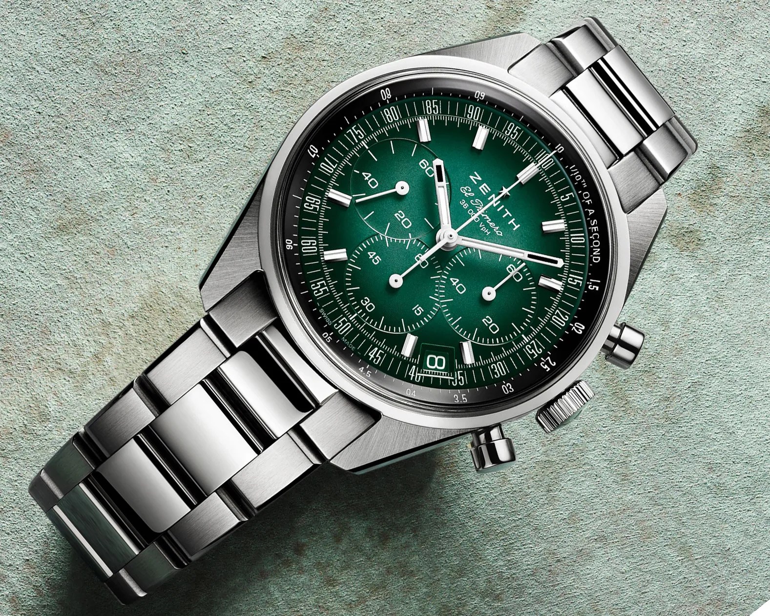 Stainless steel Zenith El Primero chronograph watch with green dial and metal bracelet on textured surface.