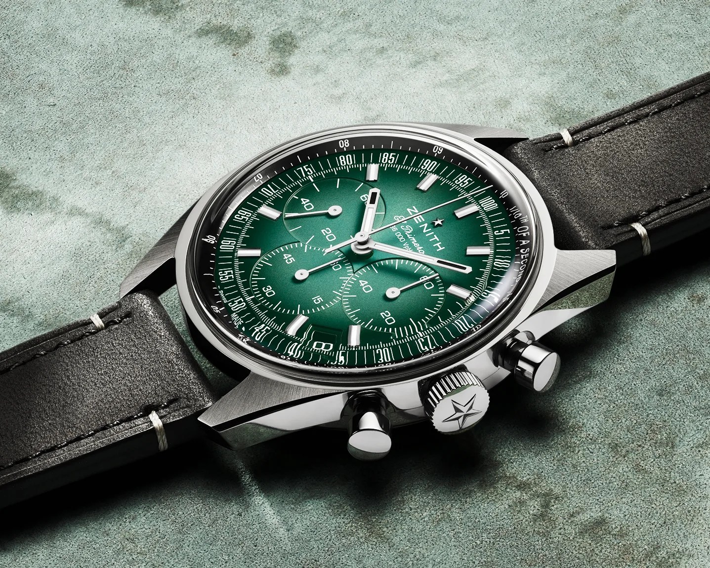 Silver Zenith chronograph watch with green dial and black leather strap on a textured green surface.