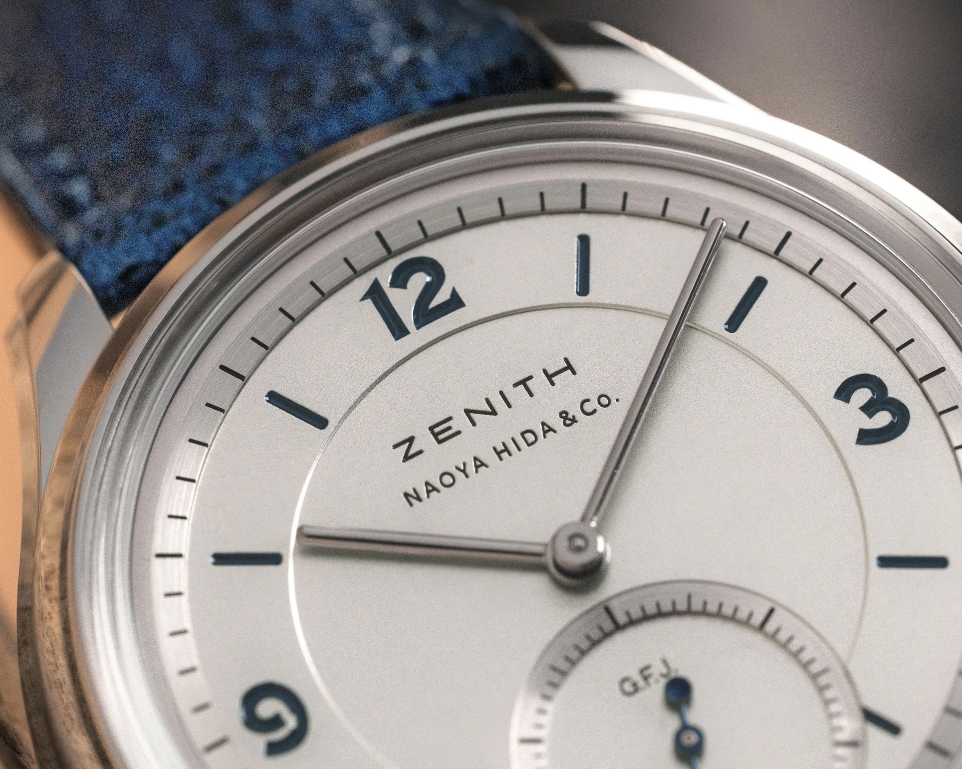 Close-up of a silver Zenith Naoya Hida & Co. watch dial with blue numerals and a blue leather strap.