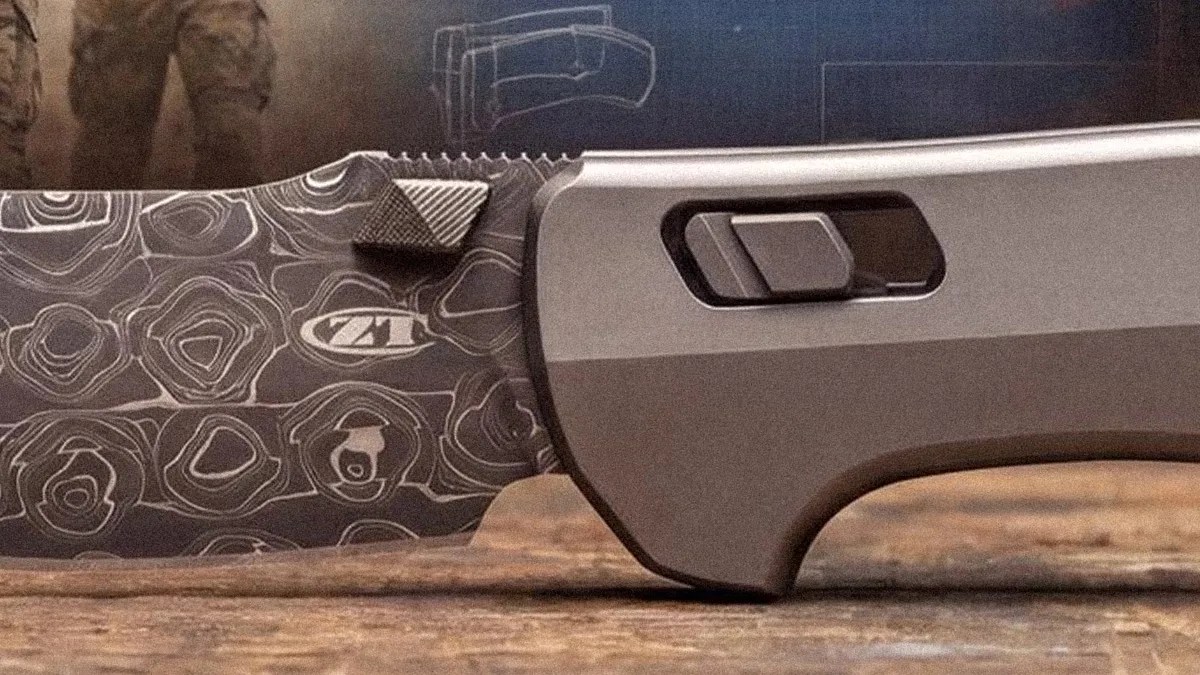 Close-up of a folding knife with a patterned blade and a metallic handle featuring a rectangular button.