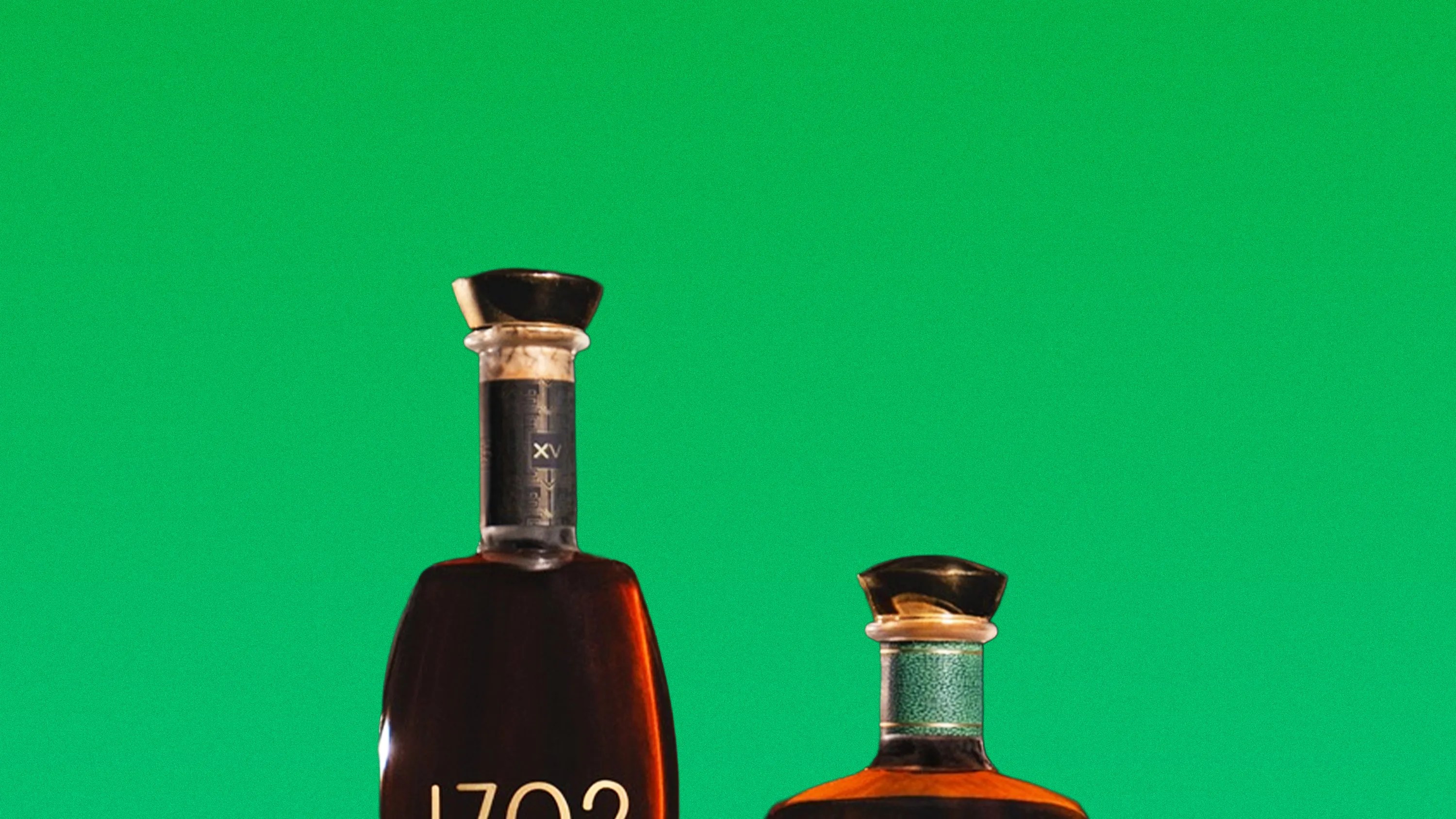 Two liquor bottles with black caps against a green background, one taller with "1702" on the label.