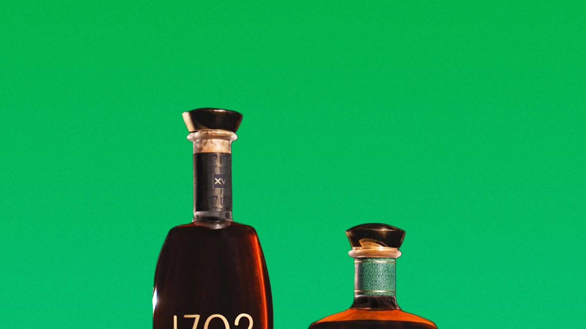 Two liquor bottles with black caps against a green background, one taller with "1702" on the label.