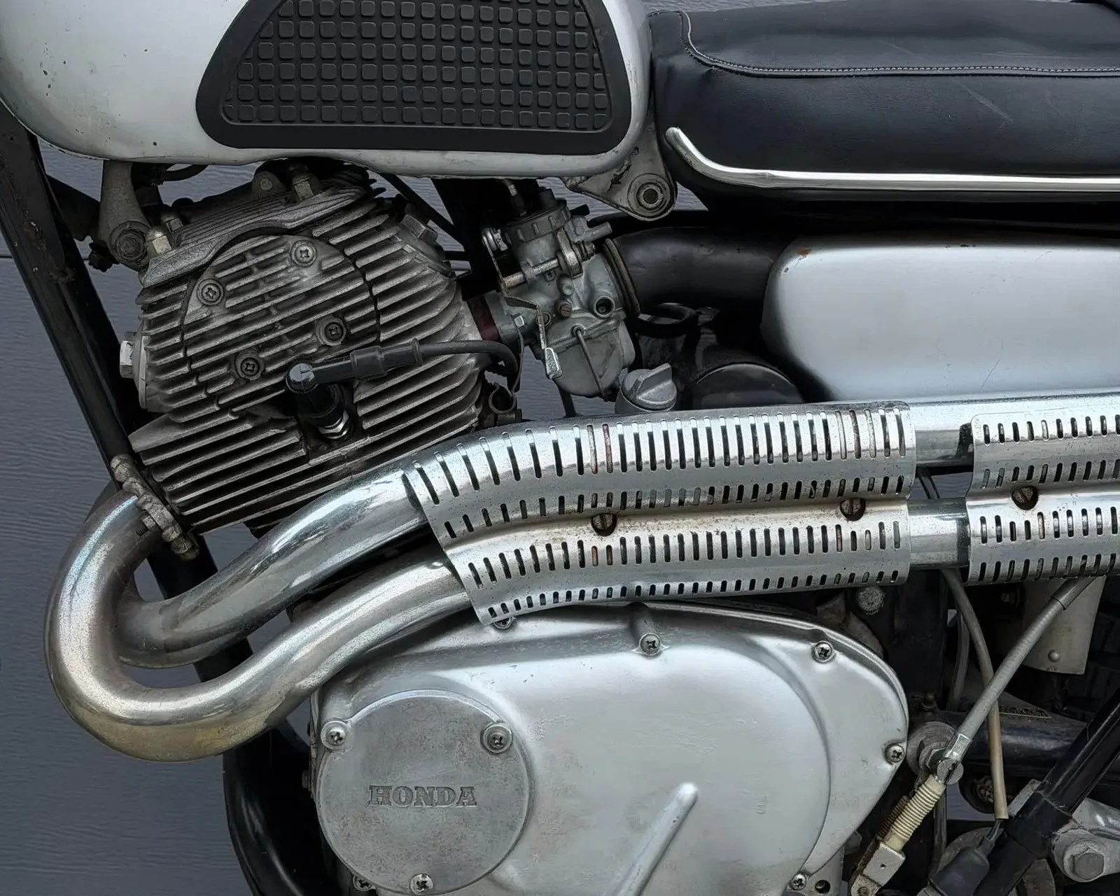 Close-up of a silver Honda motorcycle engine with visible exhaust pipes and black seat edge.