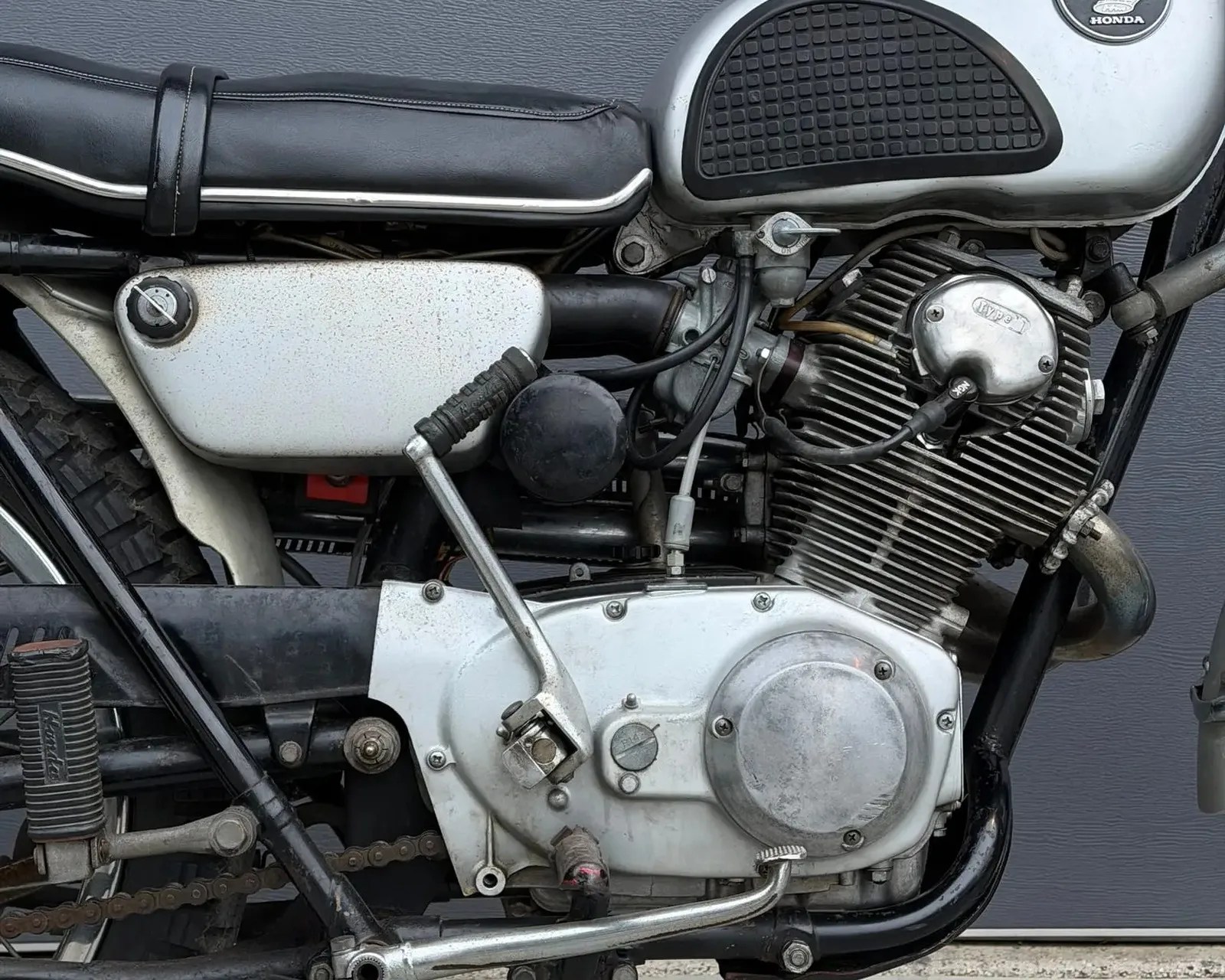 Close-up of a vintage Honda motorcycle engine with visible kickstarter, chain, and black leather seat.