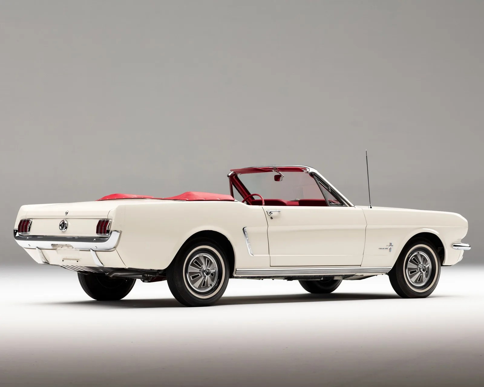 White classic Ford Mustang convertible with red interior and top down, shown from the rear side.