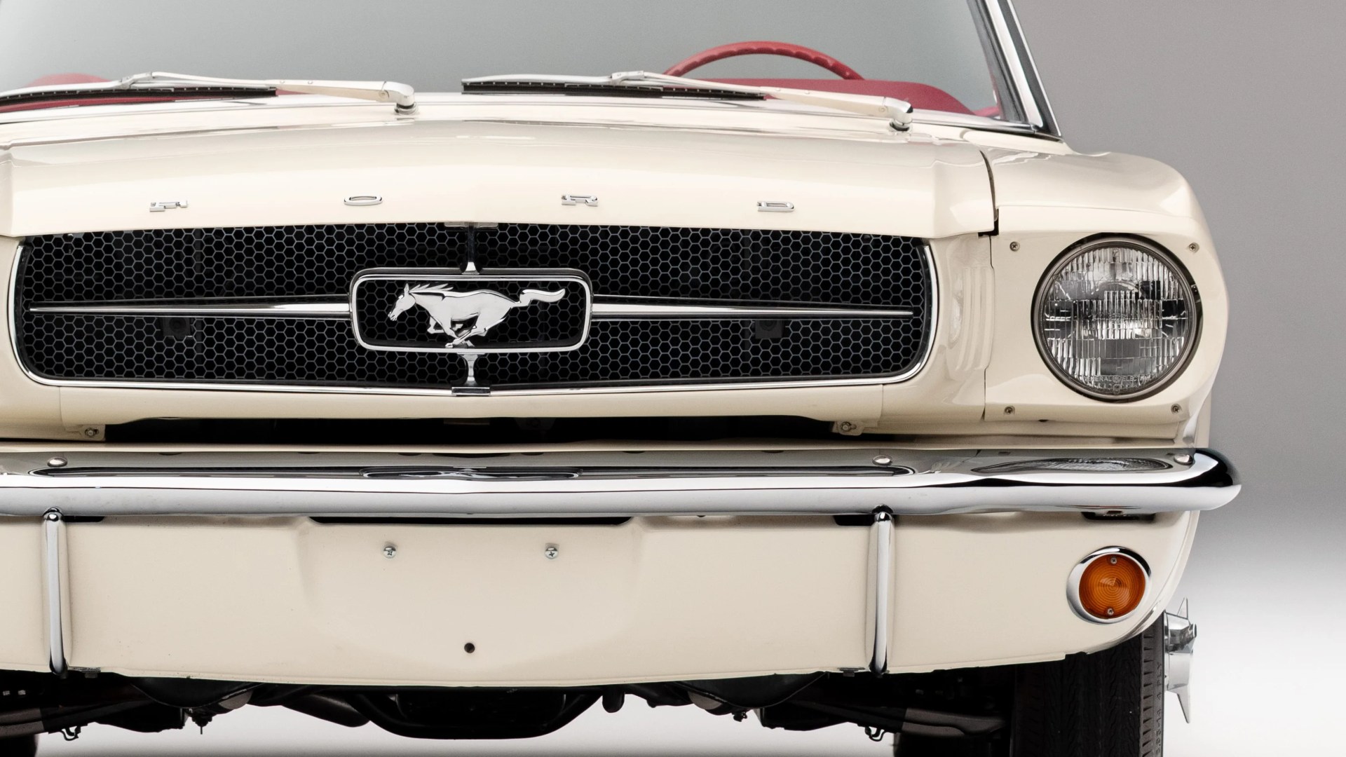 Front grille of a white classic Ford Mustang with chrome bumper and round headlight.