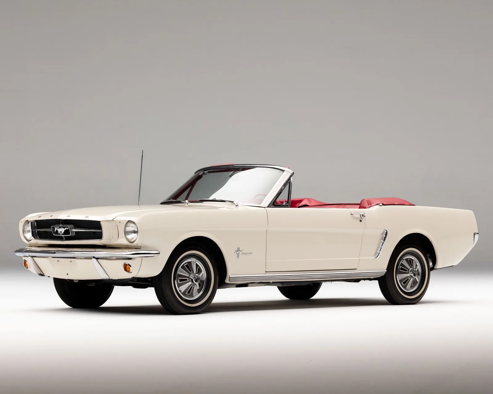 Cream-colored classic Ford Mustang convertible with red interior and chrome detailing on a neutral background.