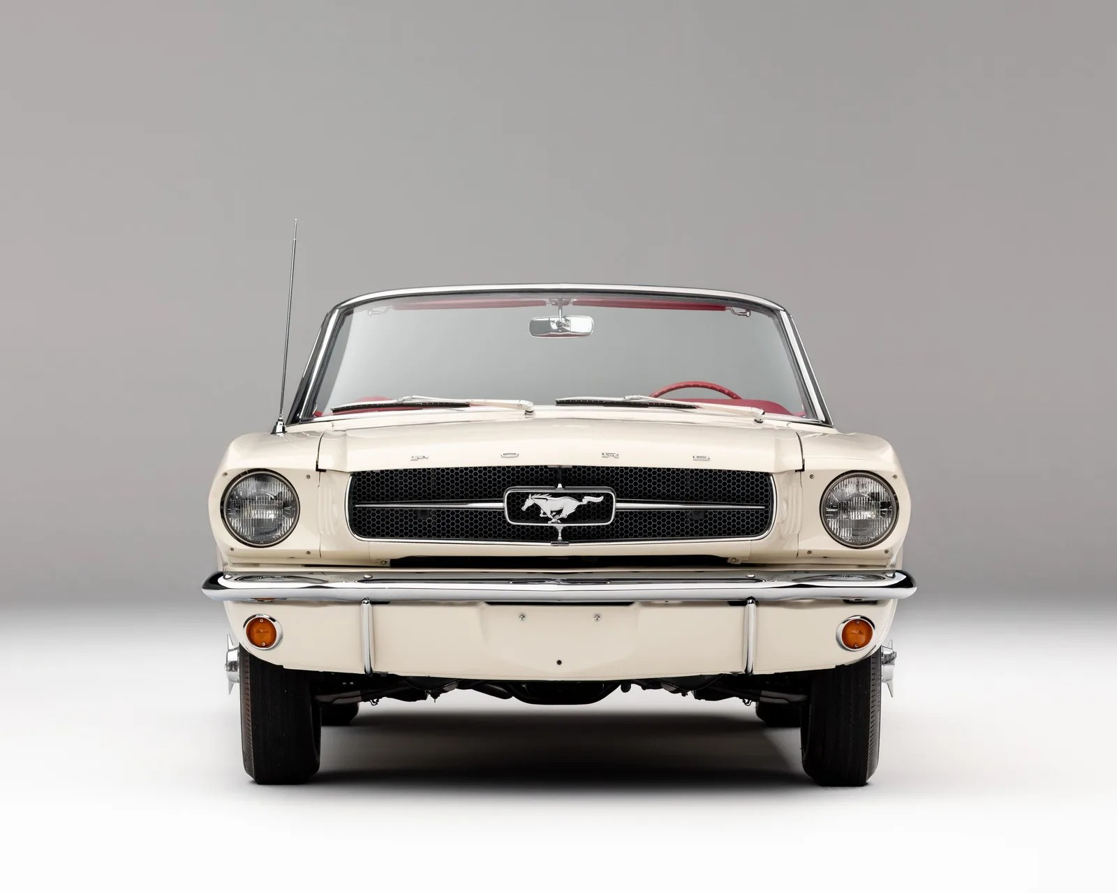 Front view of a white classic Ford Mustang convertible with a red interior and chrome bumper.