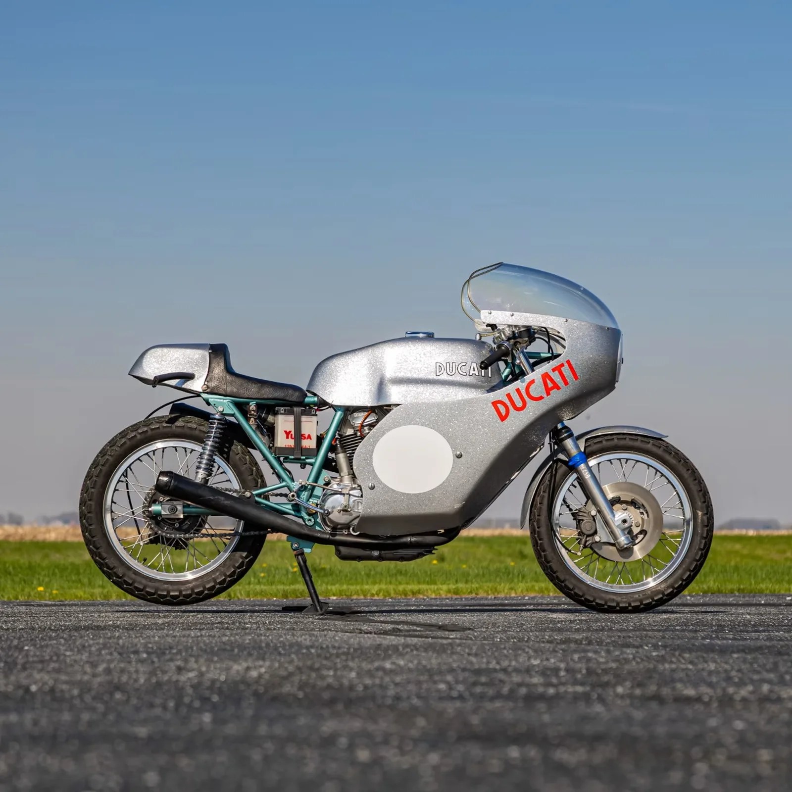 Silver vintage Ducati racing motorcycle with full fairing and black exhaust pipes on a paved surface.