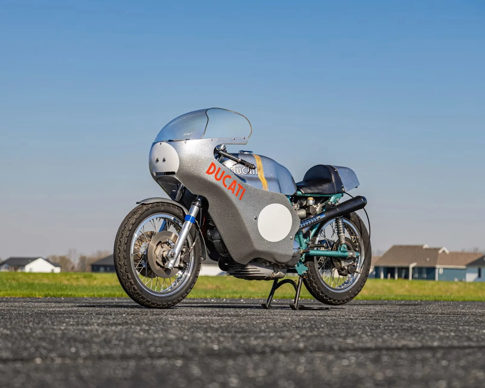 Silver vintage Ducati racing motorcycle with full fairing and red logo on a paved surface.