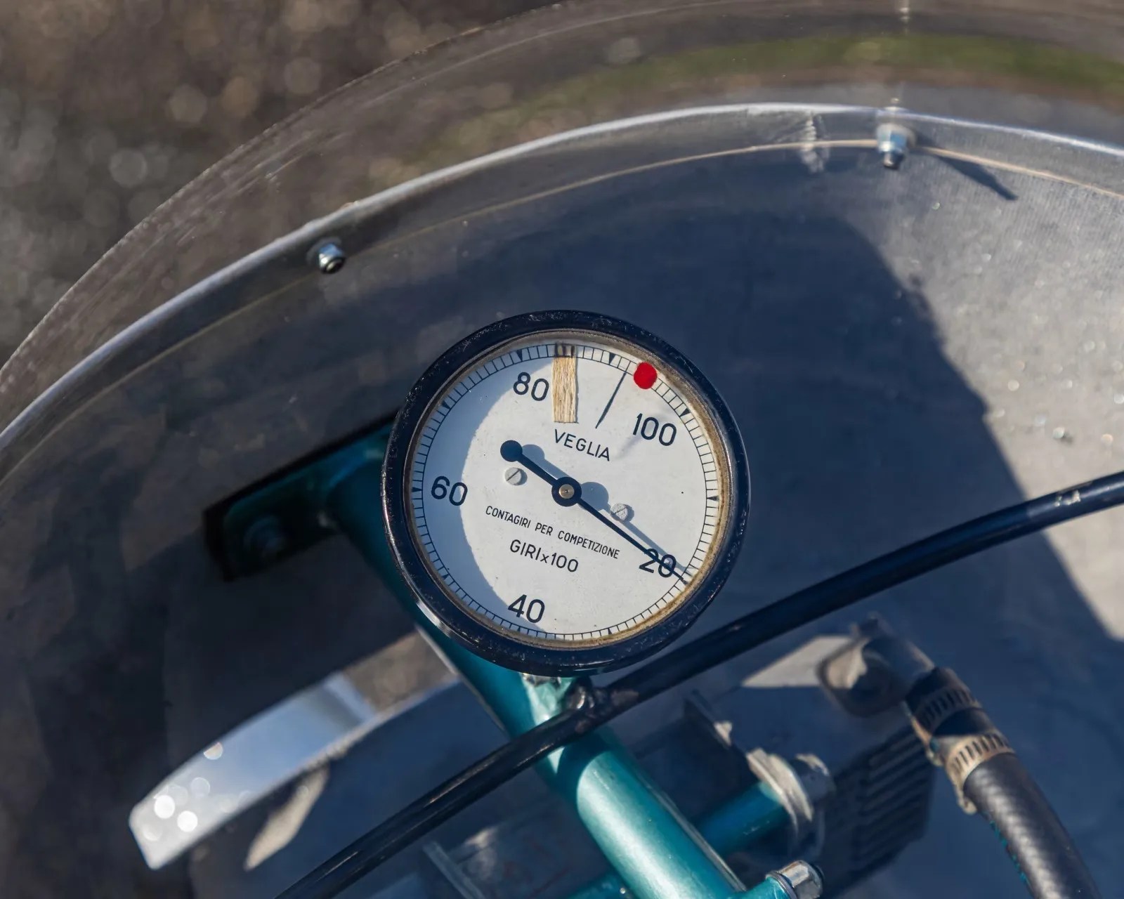 Round Veglia tachometer gauge with white face and black numbers mounted on a teal metal frame.