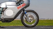 Silver Ducati motorcycle front wheel and part of the body with red Ducati logo on a road with grass background.