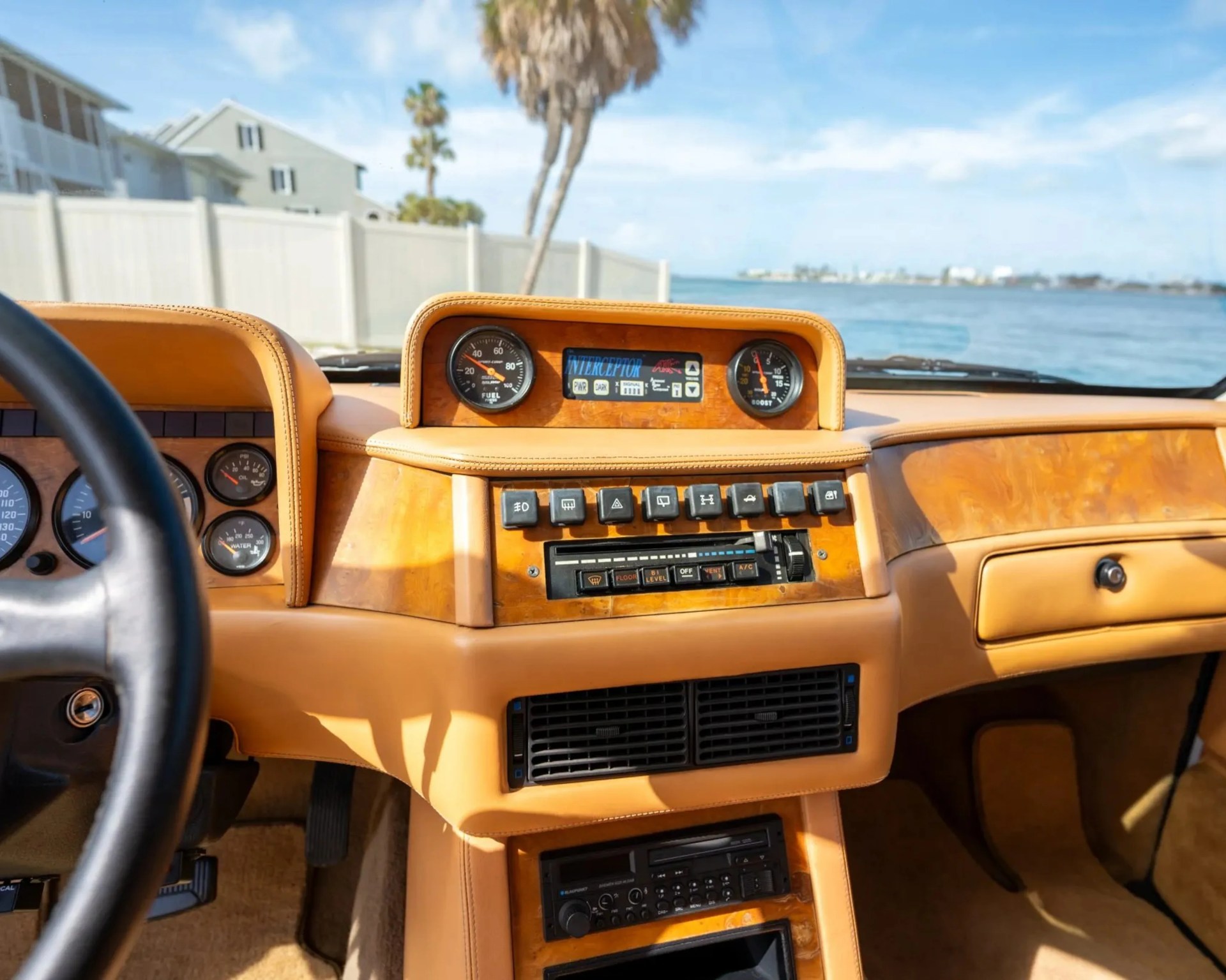 Car dashboard with tan leather and wood trim, featuring fuel and boost gauges, climate controls, and a Blaupunkt radio.