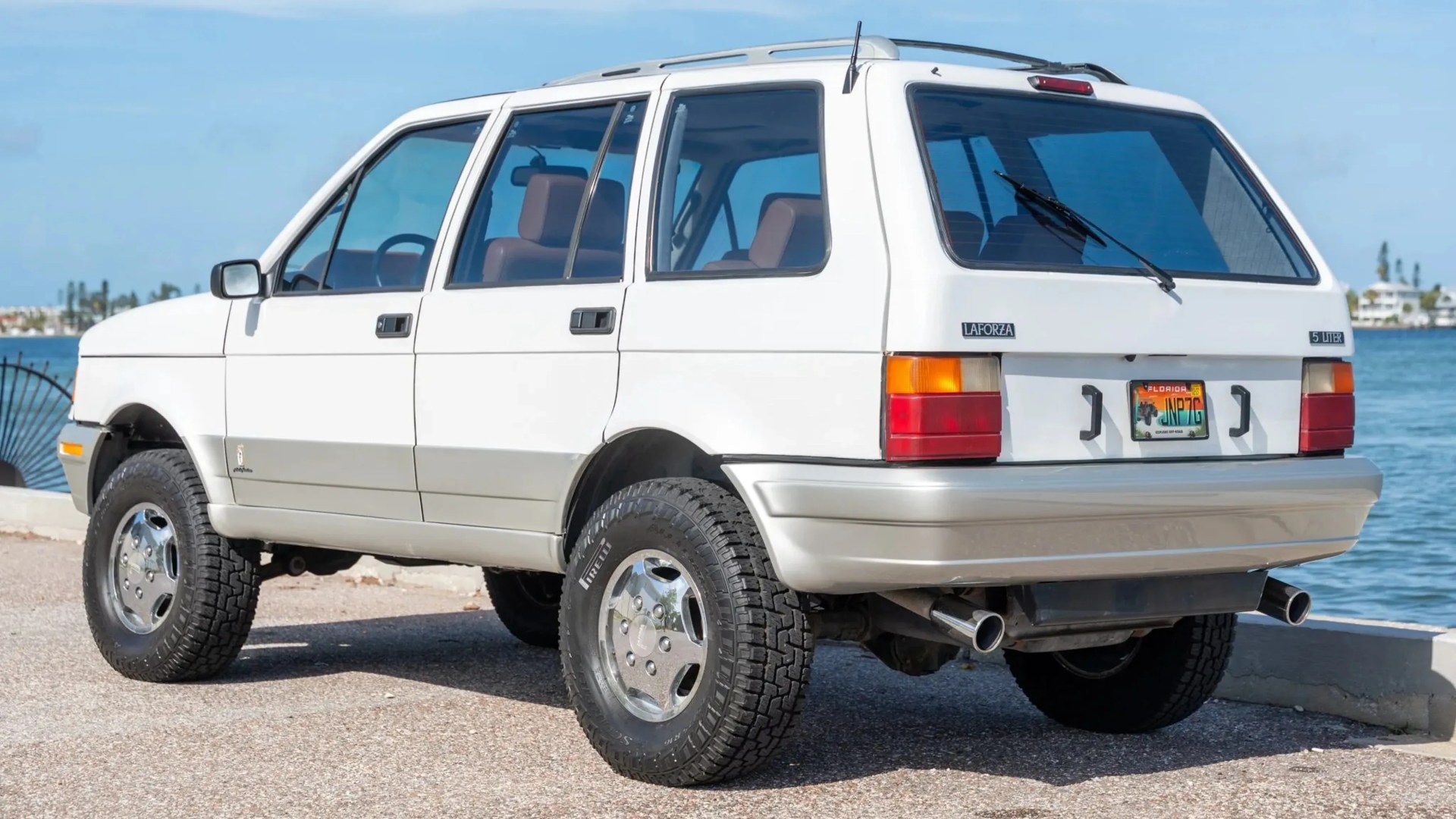 White vintage LaForza 5-liter SUV with chrome wheels parked near water.