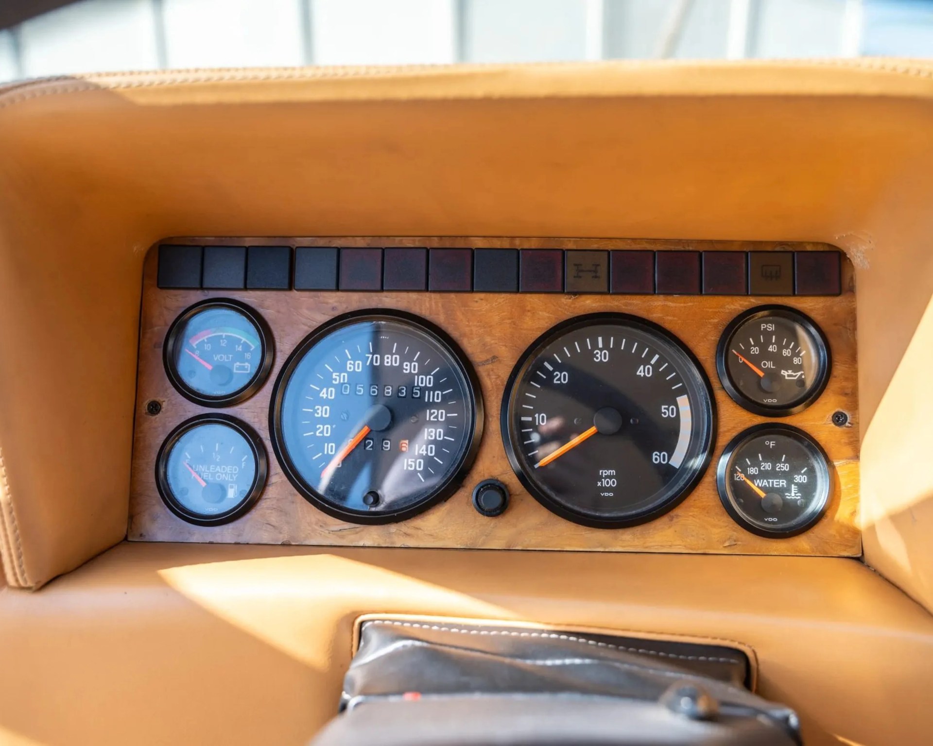 Wooden dashboard panel with analog gauges for speed, rpm, oil pressure, water temperature, and voltage in a tan interior.