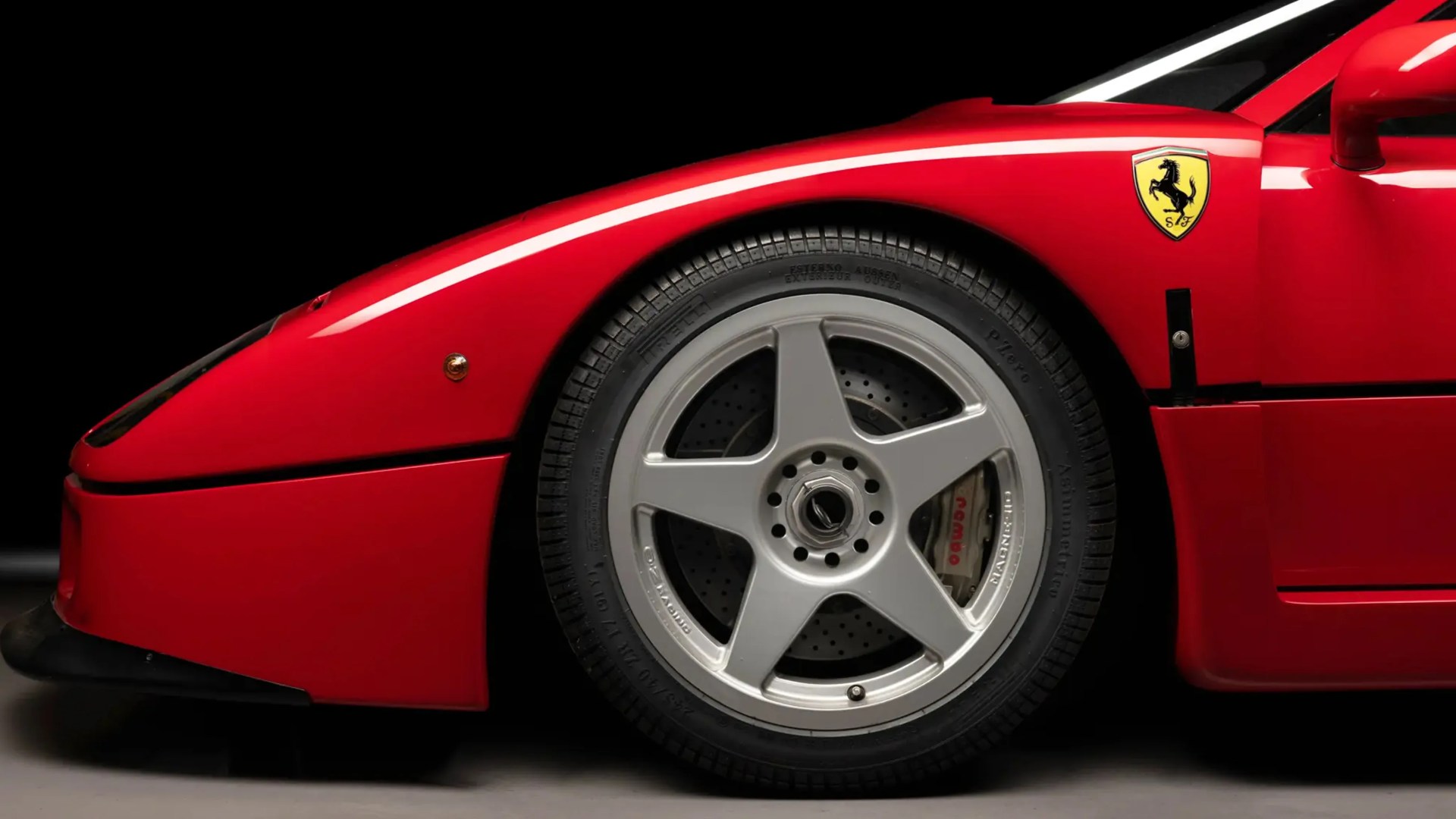 Close-up of a red Ferrari front wheel with silver five-spoke rim and Brembo brake caliper.