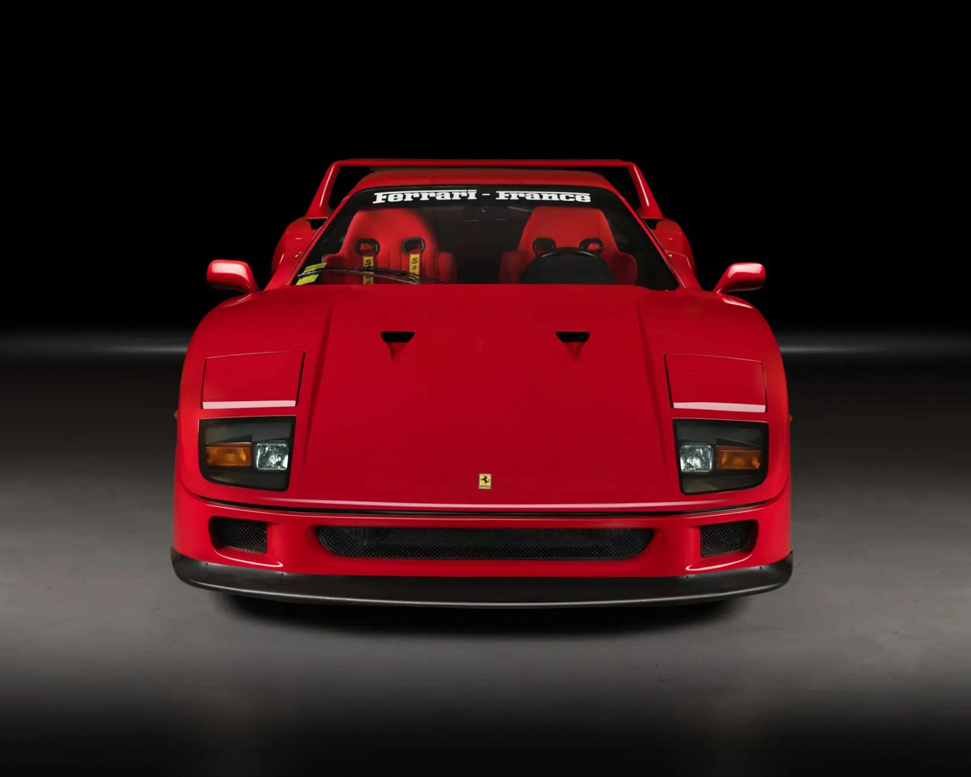 Red Ferrari sports car front view with "Ferrari - France" decal on windshield and racing seats inside.