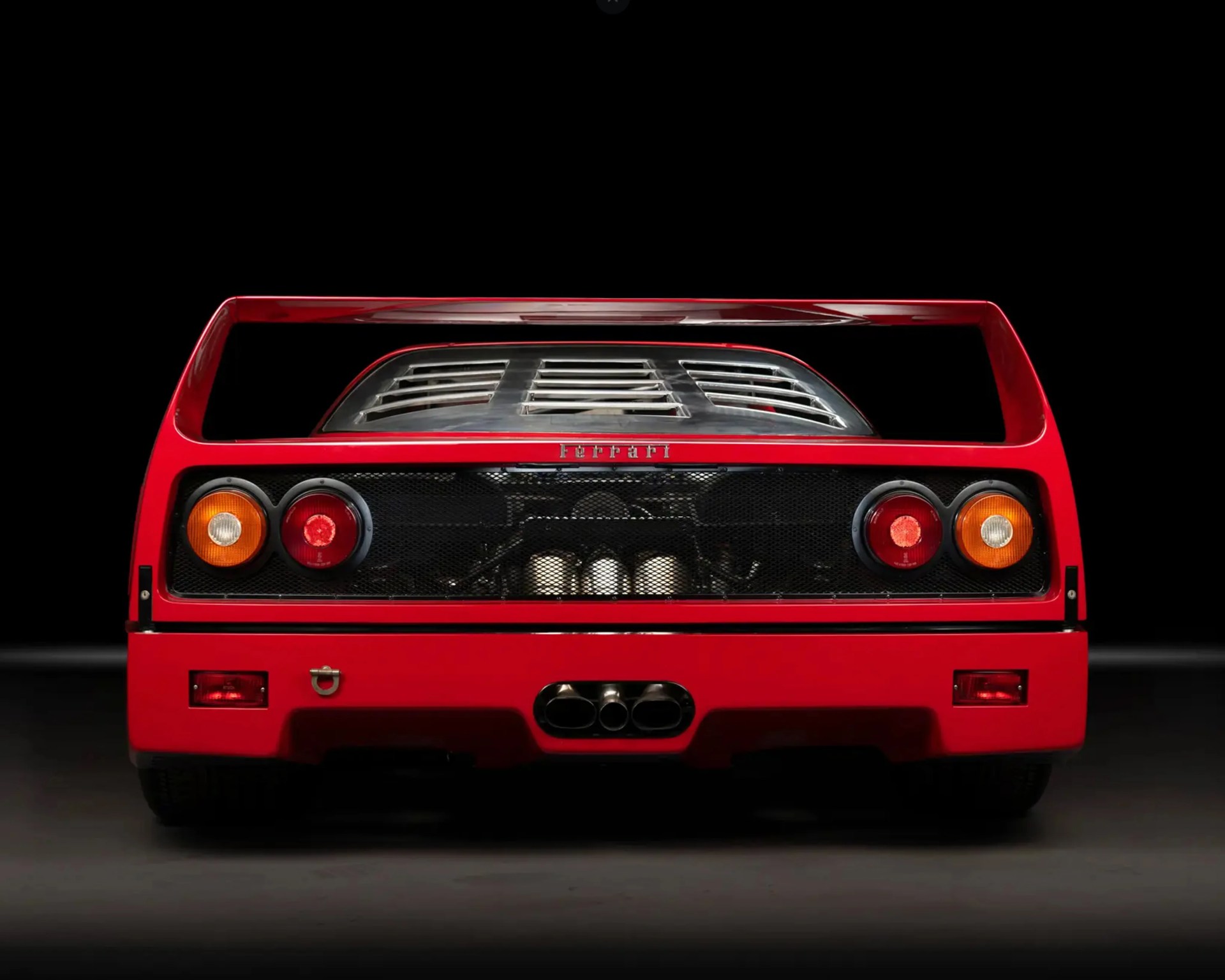 Rear view of a red Ferrari F40 showing tail lights, rear grille, exhaust pipes, and rear wing.