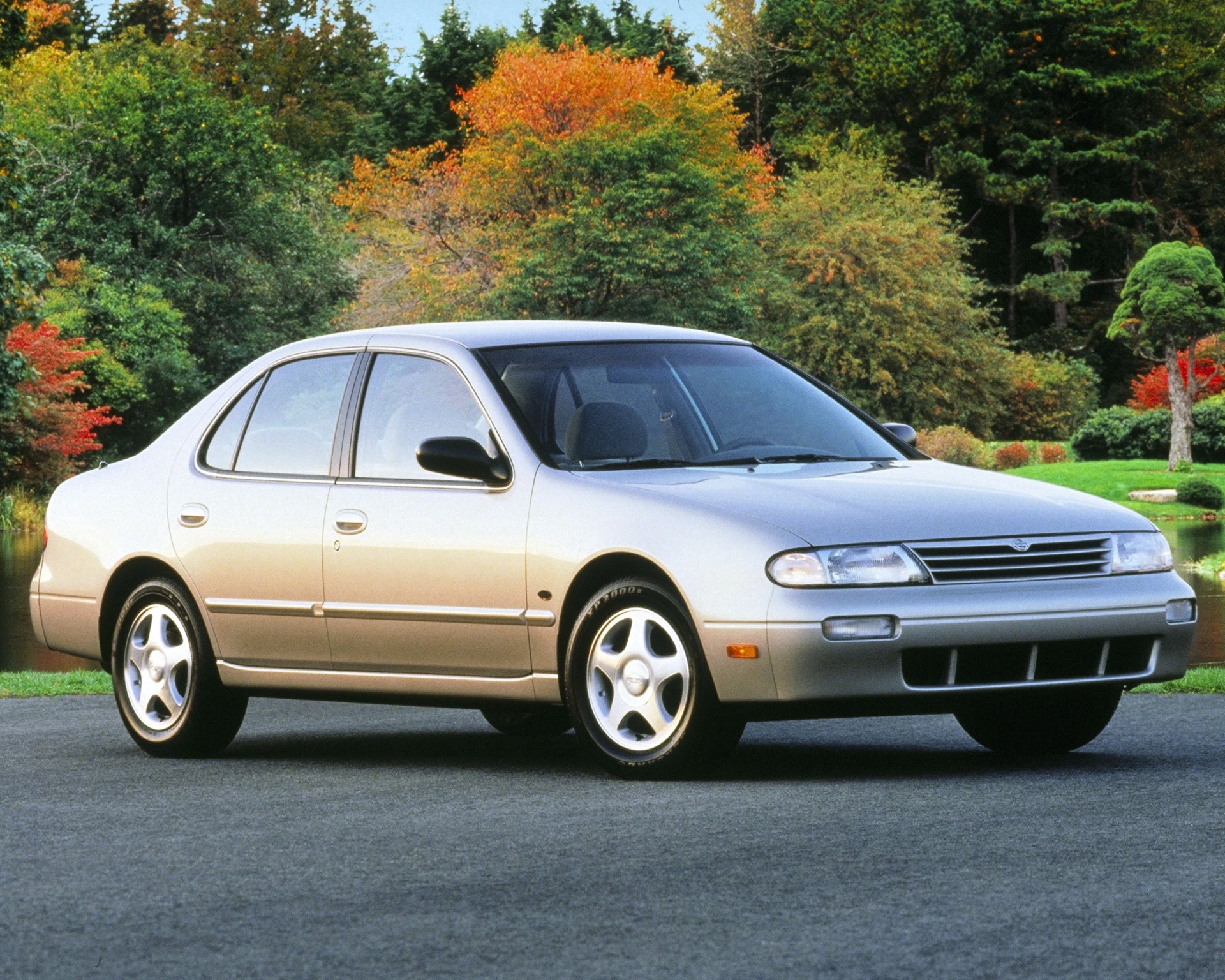 Silver four-door sedan parked on a road with autumn trees in the background.