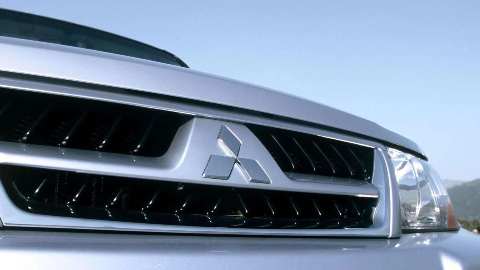 Close-up of a silver Mitsubishi car grille with the Mitsubishi logo and part of a headlight.
