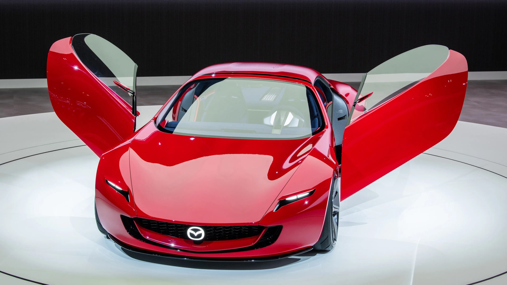 Red Mazda sports car with butterfly doors open on a white circular platform.