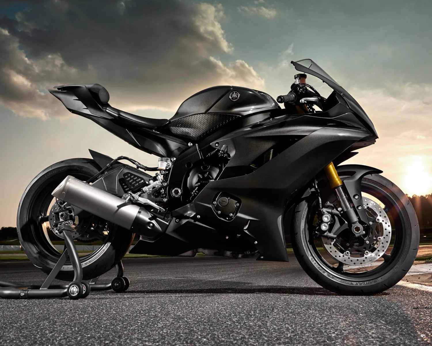 Matte black Yamaha sport motorcycle on a stand with sunset and cloudy sky in the background.