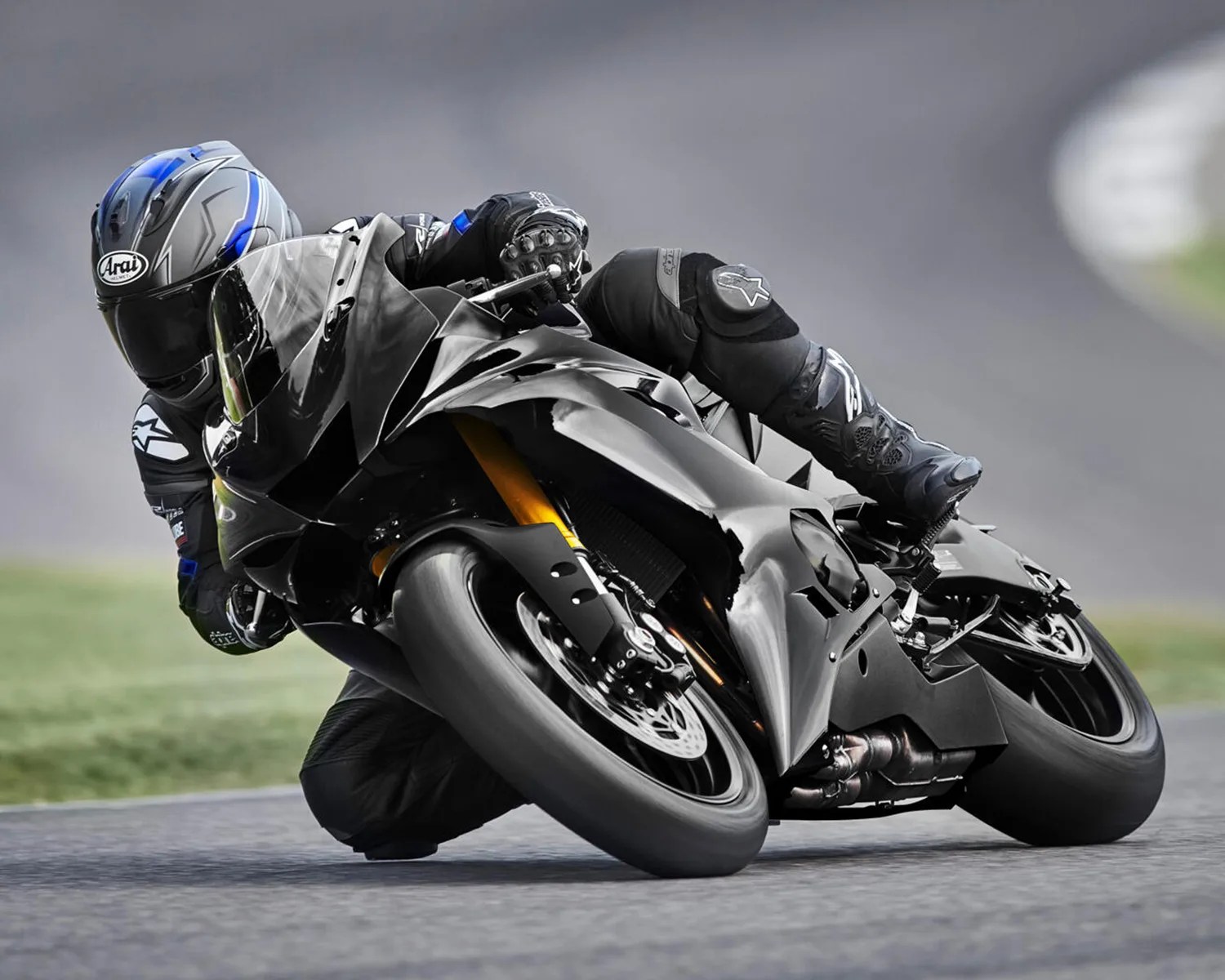 Motorcyclist in black gear and blue-accented helmet leaning into a turn on a black sportbike.