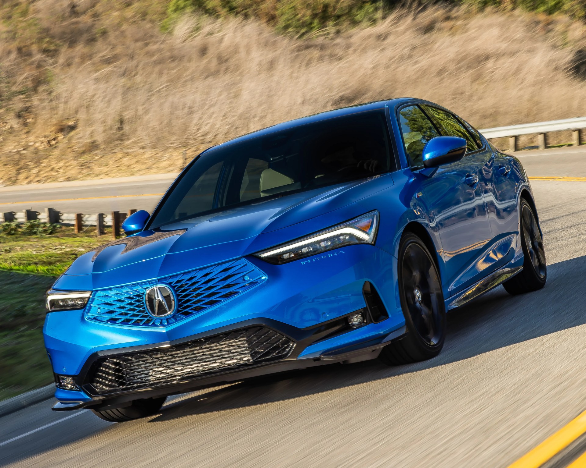 Blue Acura sedan with blacked-out windows driving on a curving road with dry grass in the background.