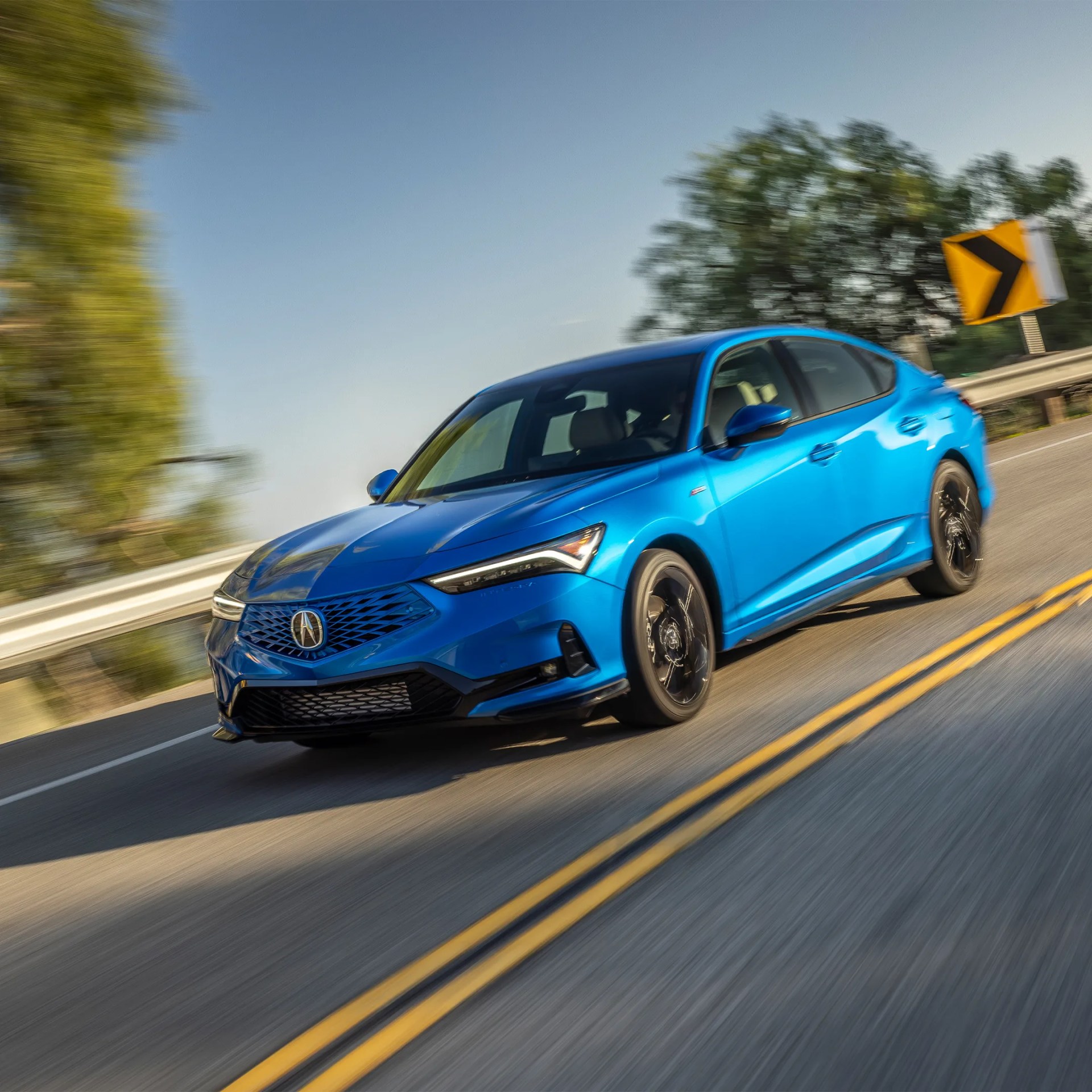 Blue Acura sedan driving on a curved road with a yellow right turn sign in the background.