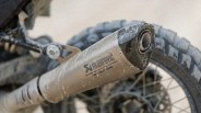 Akrapovic motorcycle exhaust pipe with dirt and mud on it, mounted on a dirt bike tire.