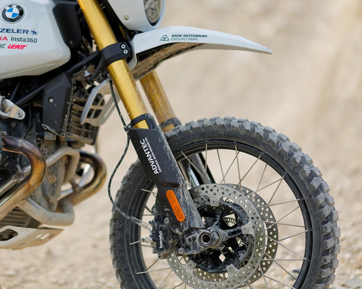 Close-up of a BMW motorcycle front wheel with knobby tire, gold suspension forks, and ADVANTEC branding on the fork guard.
