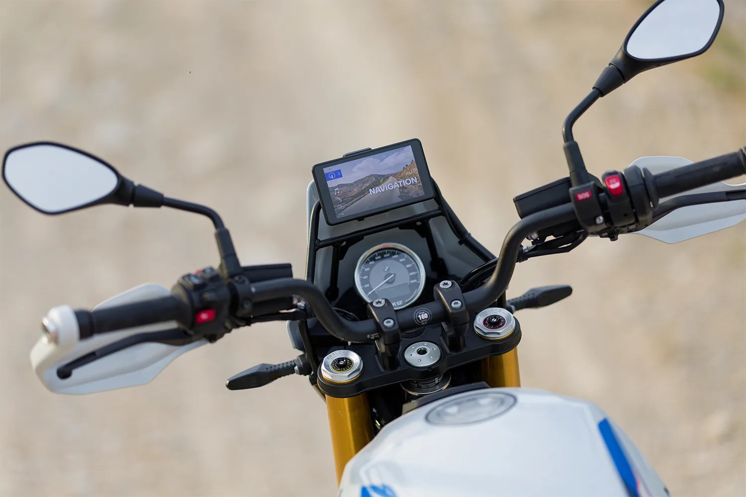 Motorcycle handlebars with rearview mirrors, a speedometer, and a navigation screen displaying a road scene.