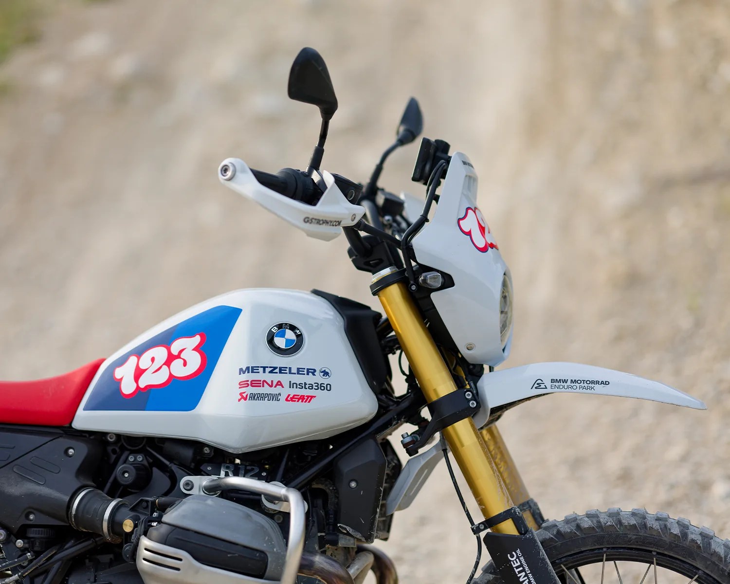 White BMW motorcycle with red seat, gold front forks, and number 123 decal on the fuel tank.