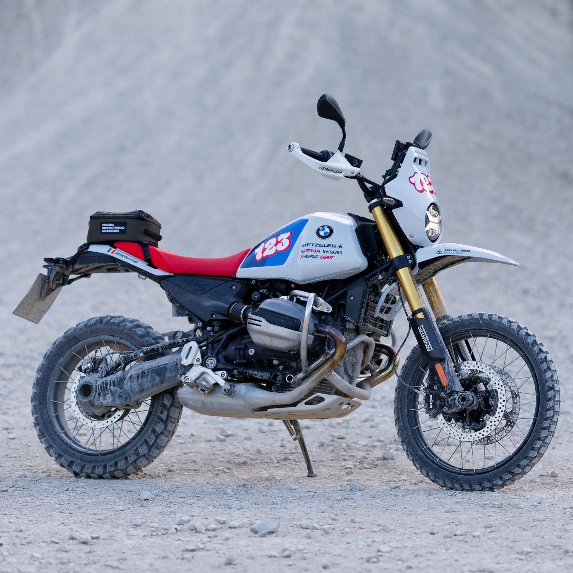 White and red BMW off-road motorcycle with knobby tires on rocky terrain.