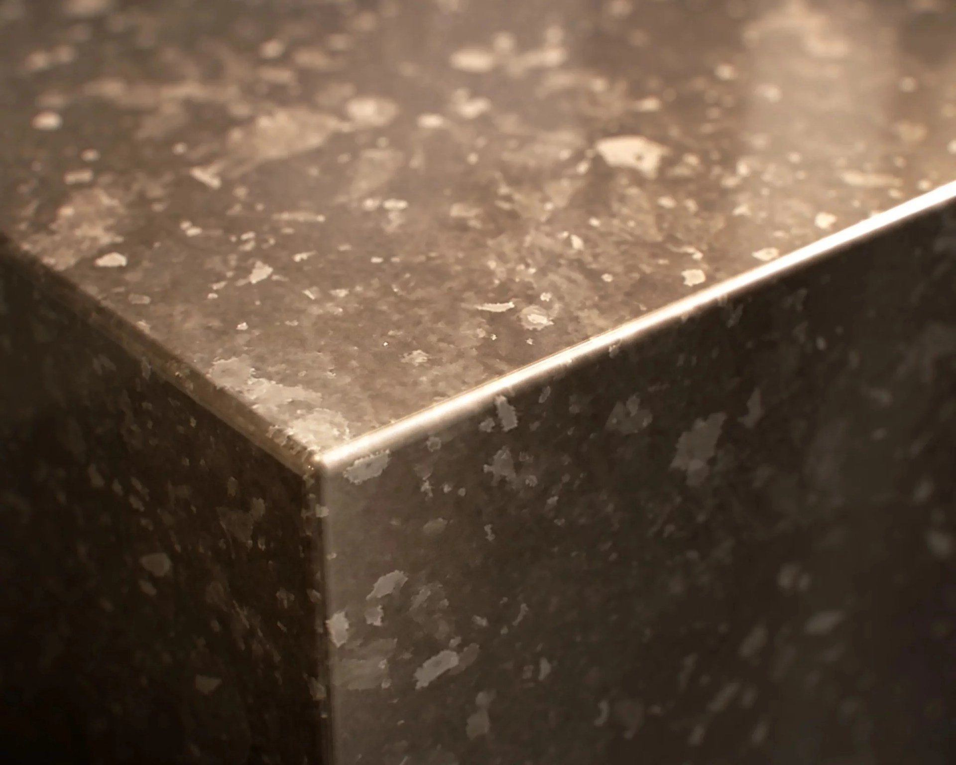 Close-up of a polished dark granite countertop corner with light gray speckles.