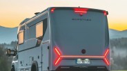 Rear view of a gray Bürstner camper van with illuminated red taillights at sunset.